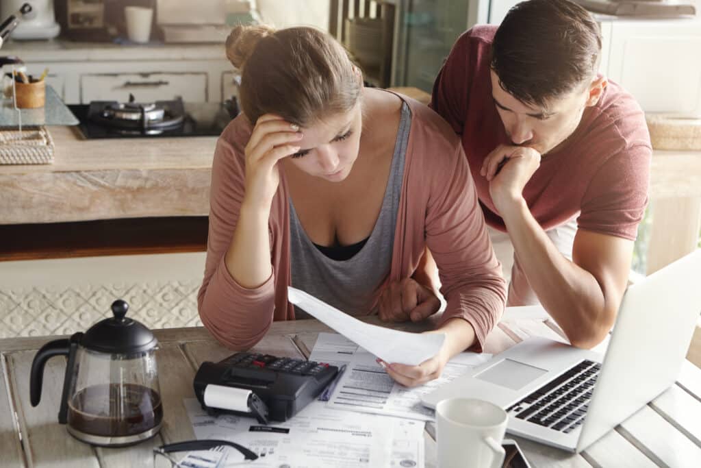 Worried couple reviewing their family finances and calculating expenses, trying to save some money t